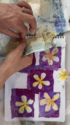 Hands creating a torn paper collage of frangipani / Plumeria flowers. Top down view