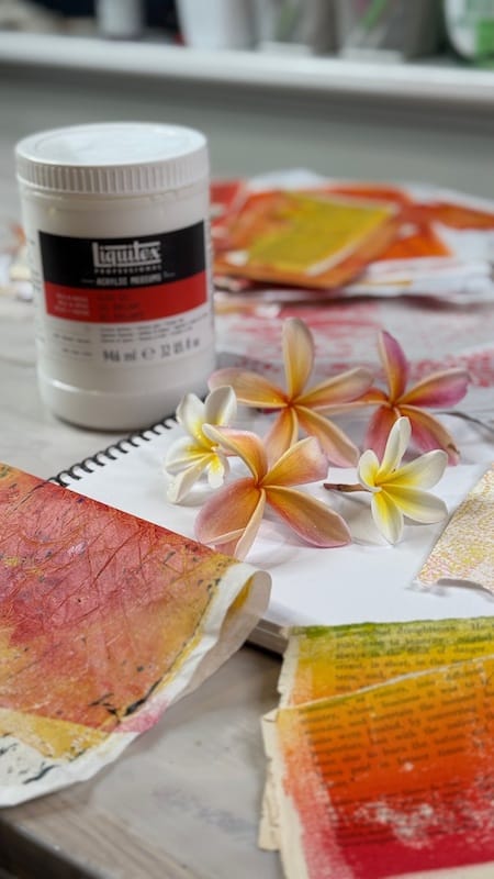Frangipani / plumeria flowers surrounded by collage papers, gel prints, gloss medium collaging glue and a brush in a pot.