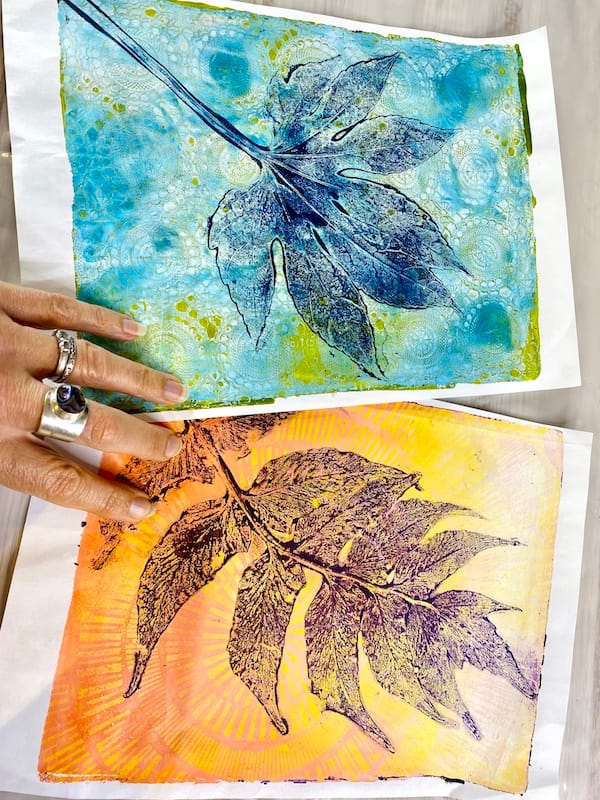 Two gel prints showing a leaf design with a patterned background. There is a hand in the picture holding the prints.