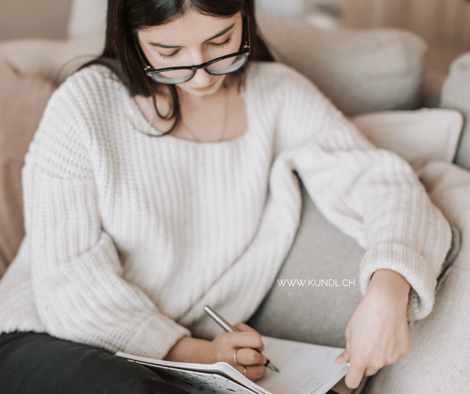 auf der Couch sitzende Frau die in ein Notizbuch schreibt