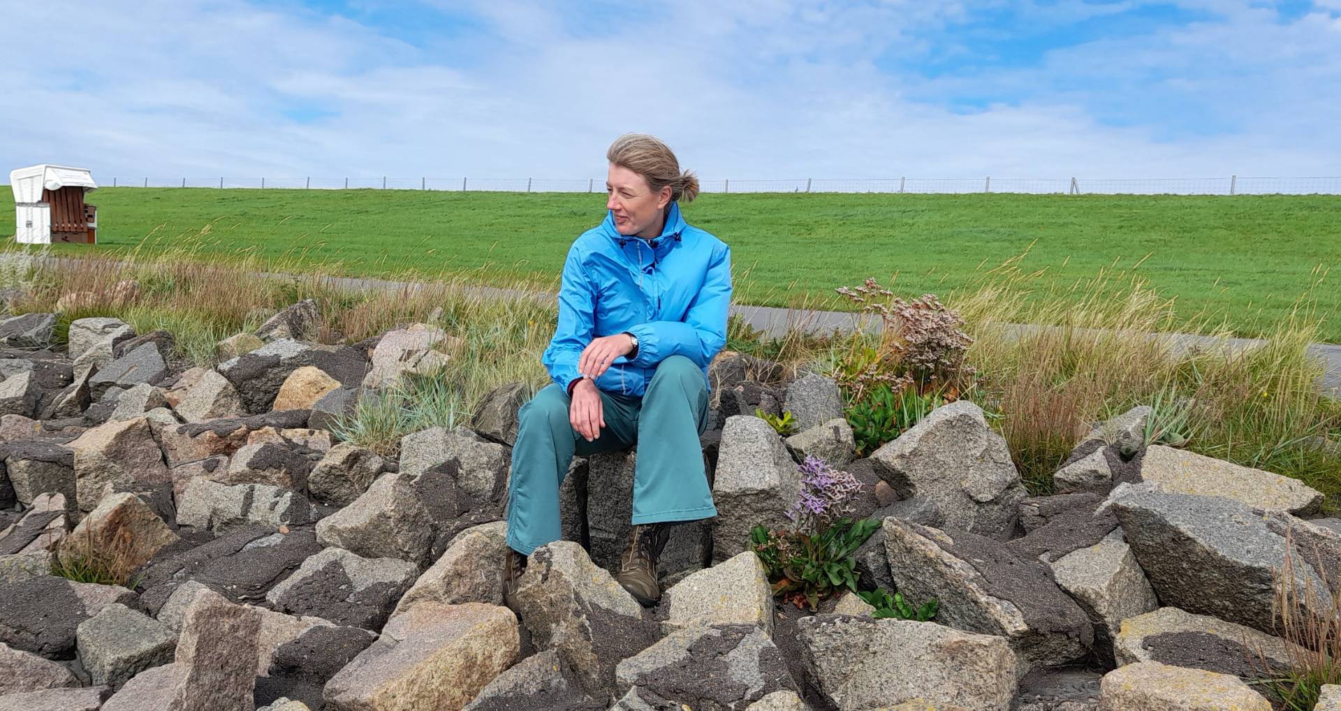Tierkommunikatorin Johanna Fleischmann sitzt auf Steinen am Meer und blickt über das Watt.