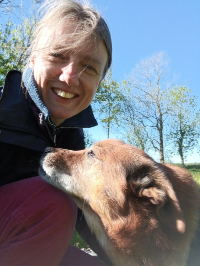Tierkommunikatorin Johanna Fleischmann streichelt ihren Hund, der vor ihr auf einer Wiese steht. 