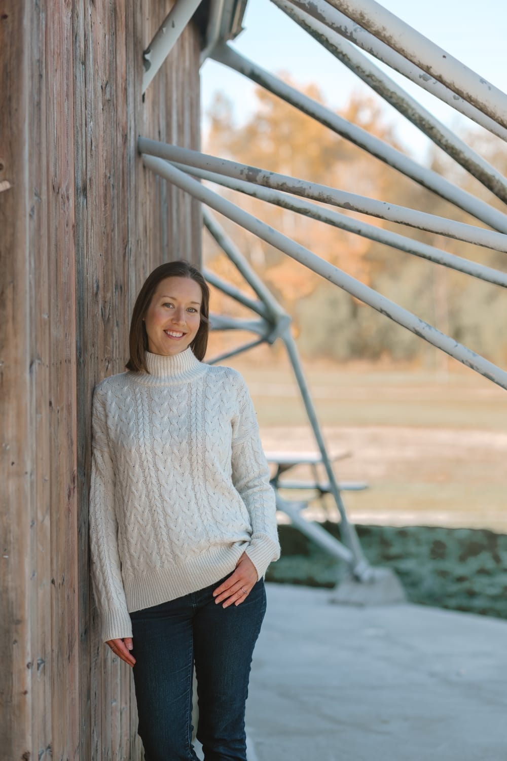 coach leaning against structure with abstract design in cozy white sweater, smiling at camera