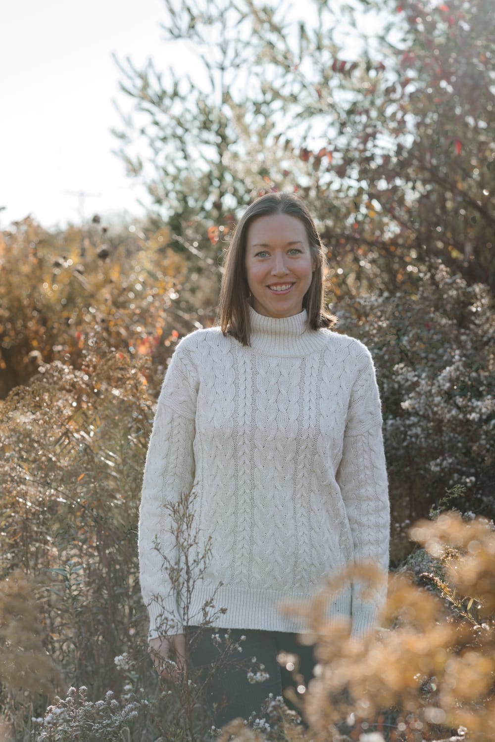 coach in cozy white sweater amongst plants in field 