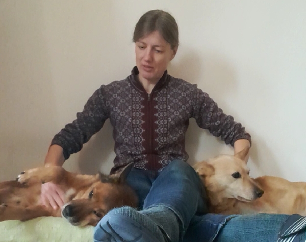 Hundetrainerin Johanna Fleischmann sitzt mit zwei Hunden auf Hundekissen im Wohnzimmer und streichelt sie beruhigend in der Silvesternacht.