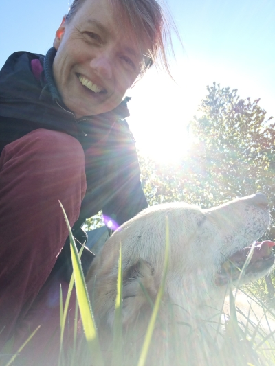 Hundetrainerin Johanna Fleischmann streichelt ihren Hund, welcher auf der Wiese liegt.