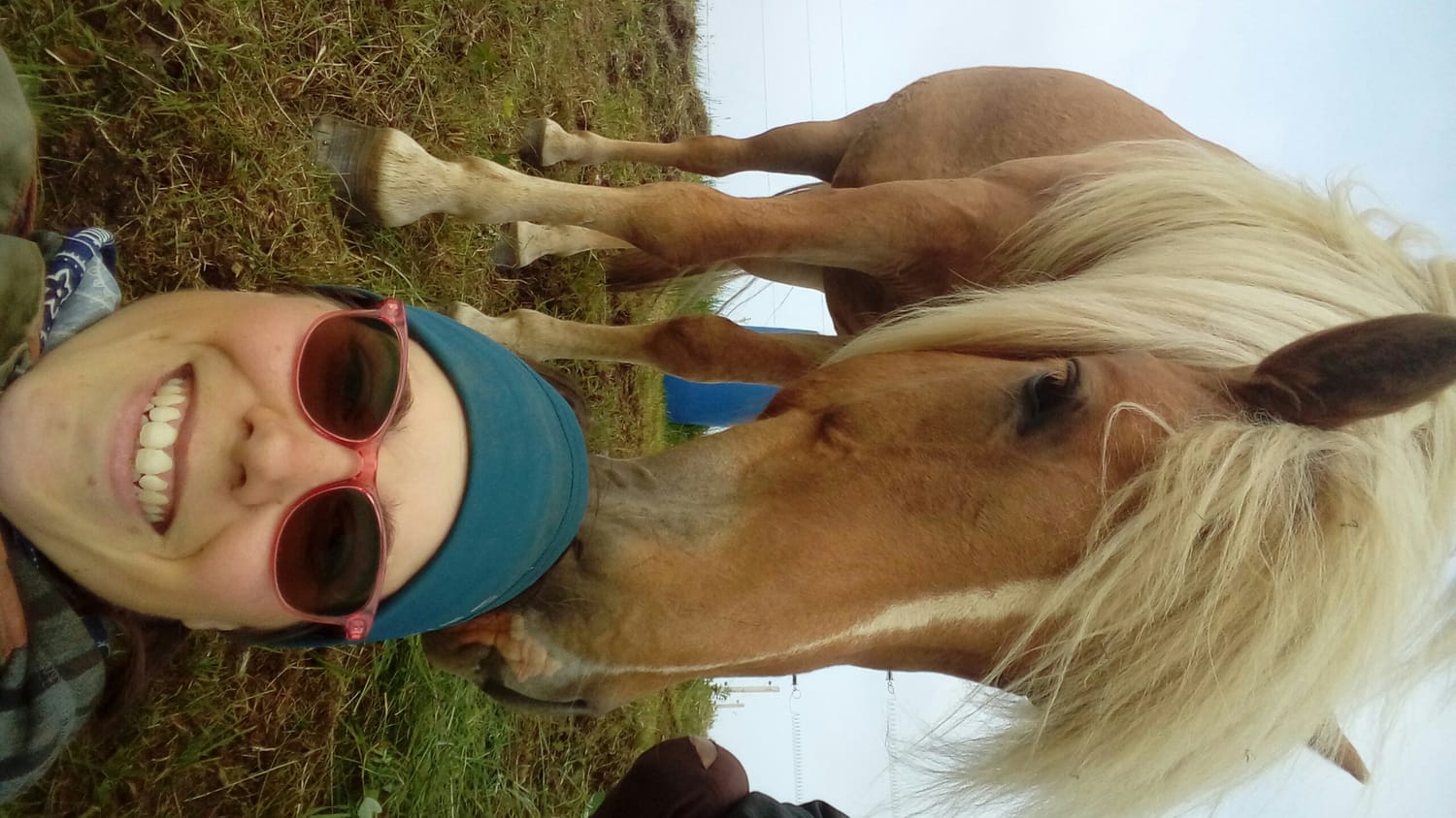 Selfie of a woman and a chestnut horse with light mane sharing a moment of connection and well-being in the grass.