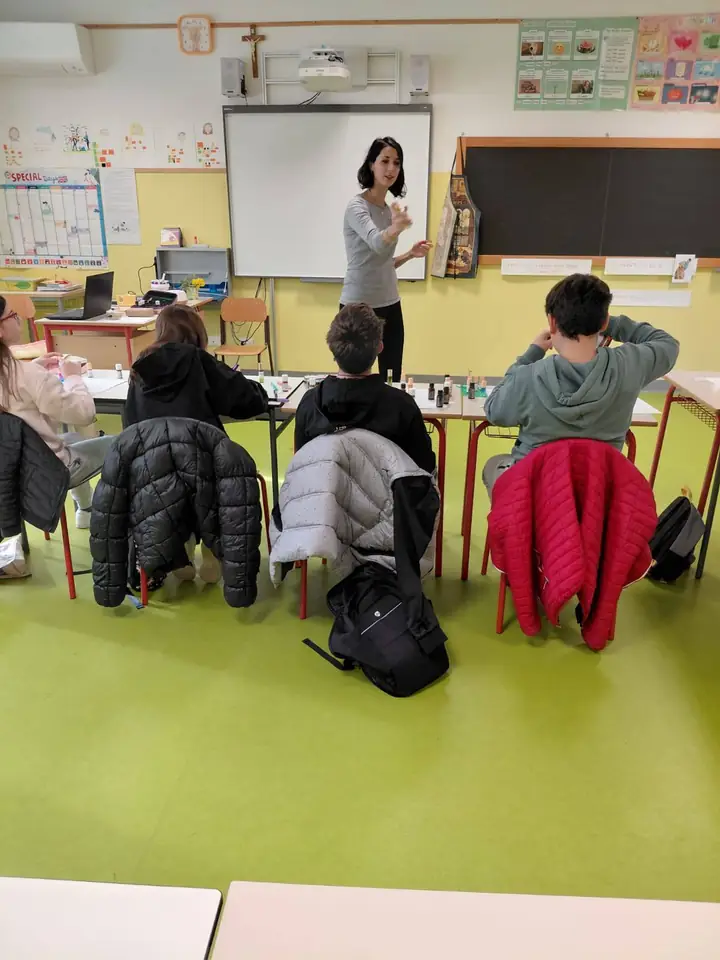 Giulia in classe davanti agli studenti con le boccette di oli sui banchi