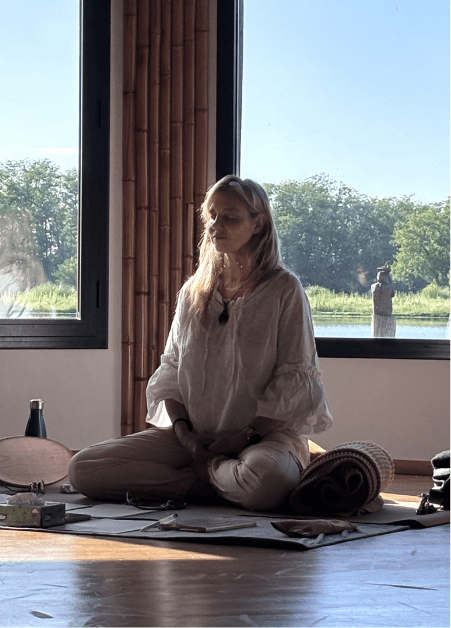 Primer plano de la mano derecha de una mujer en mudra gyan, sentada con las piernas cruzadas y usando ropa gris claro