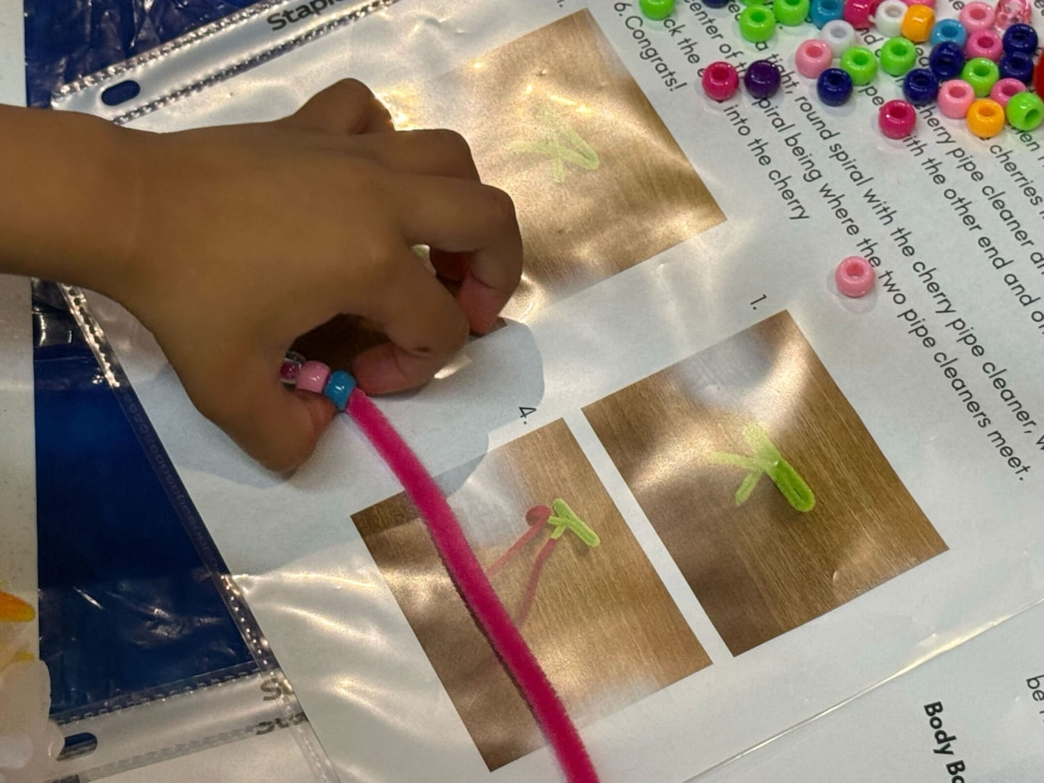 Close-up of small toddler hands threading colorful beads onto a pipe cleaner, a quiet moment of focus and early development. 