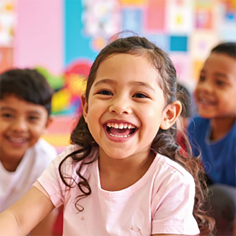 young child laughing with a classroom in the background