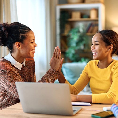 woman and girl give each other a high five while sitting at a computer