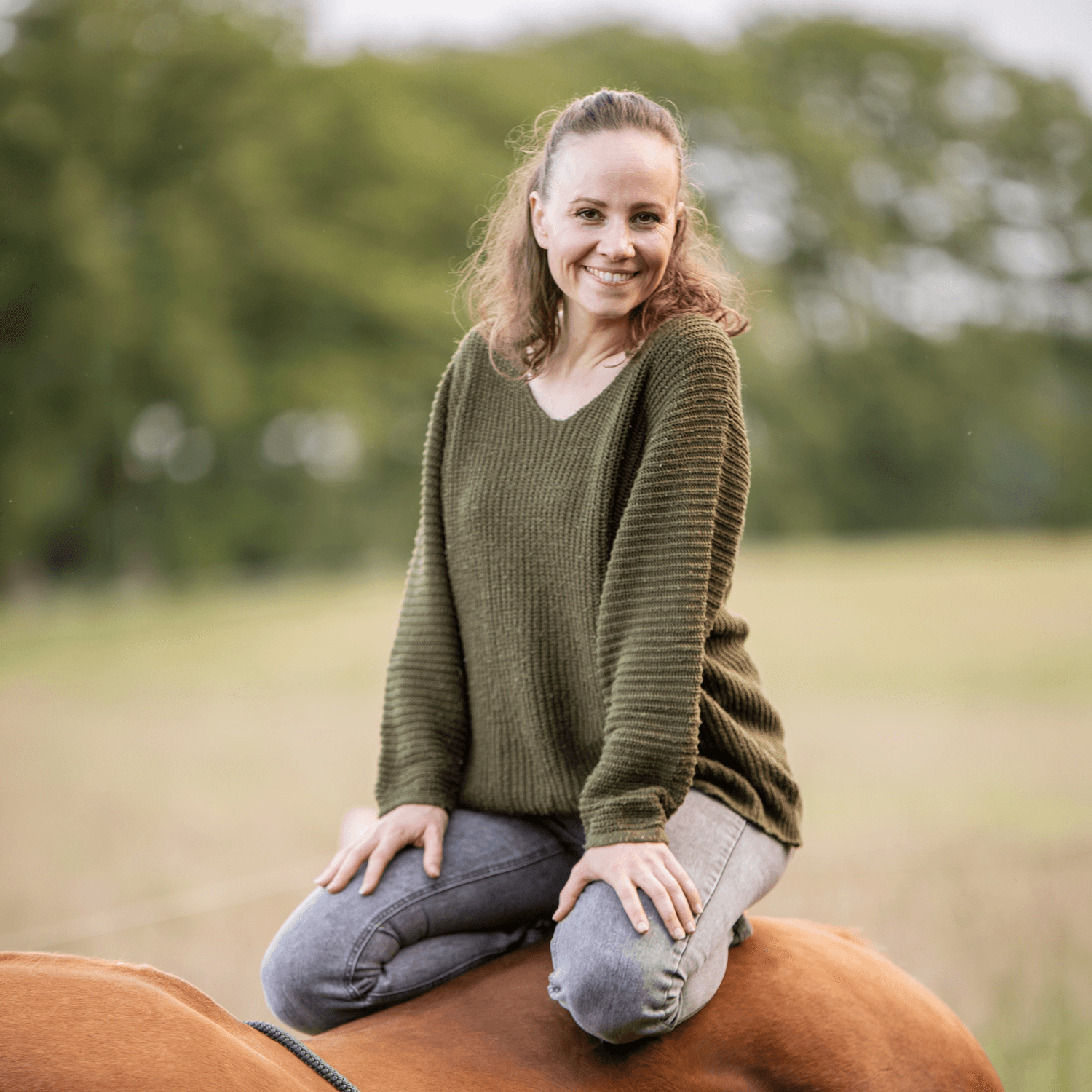 Tanja lächelt auf ihrem Pferd in der Natur