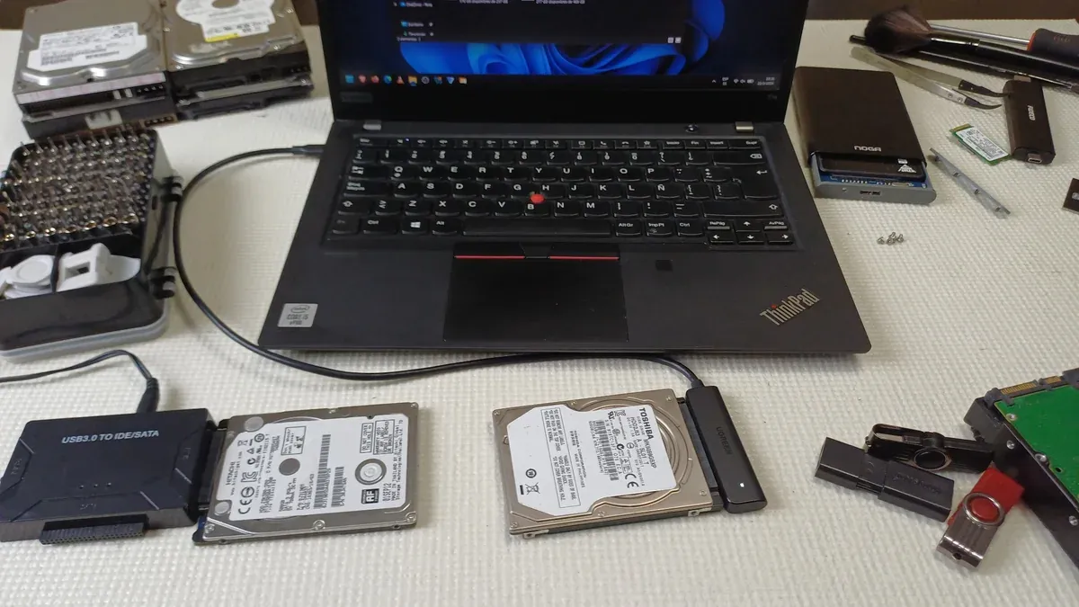 Mesa de trabajo real de KAMBIG con discos duros, adaptadores USB-SATA, memorias y una laptop para diagnóstico y recuperación de datos