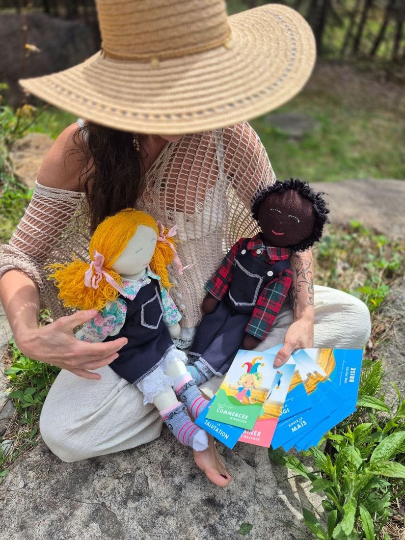 Les poupées Guillaume et Charlotte assises sur une roche en forêt, avec les cartes de manœuvres de massage.
