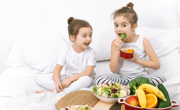 Deux soeurs qui rient en mangeant des fruits et l&eacute;gumes