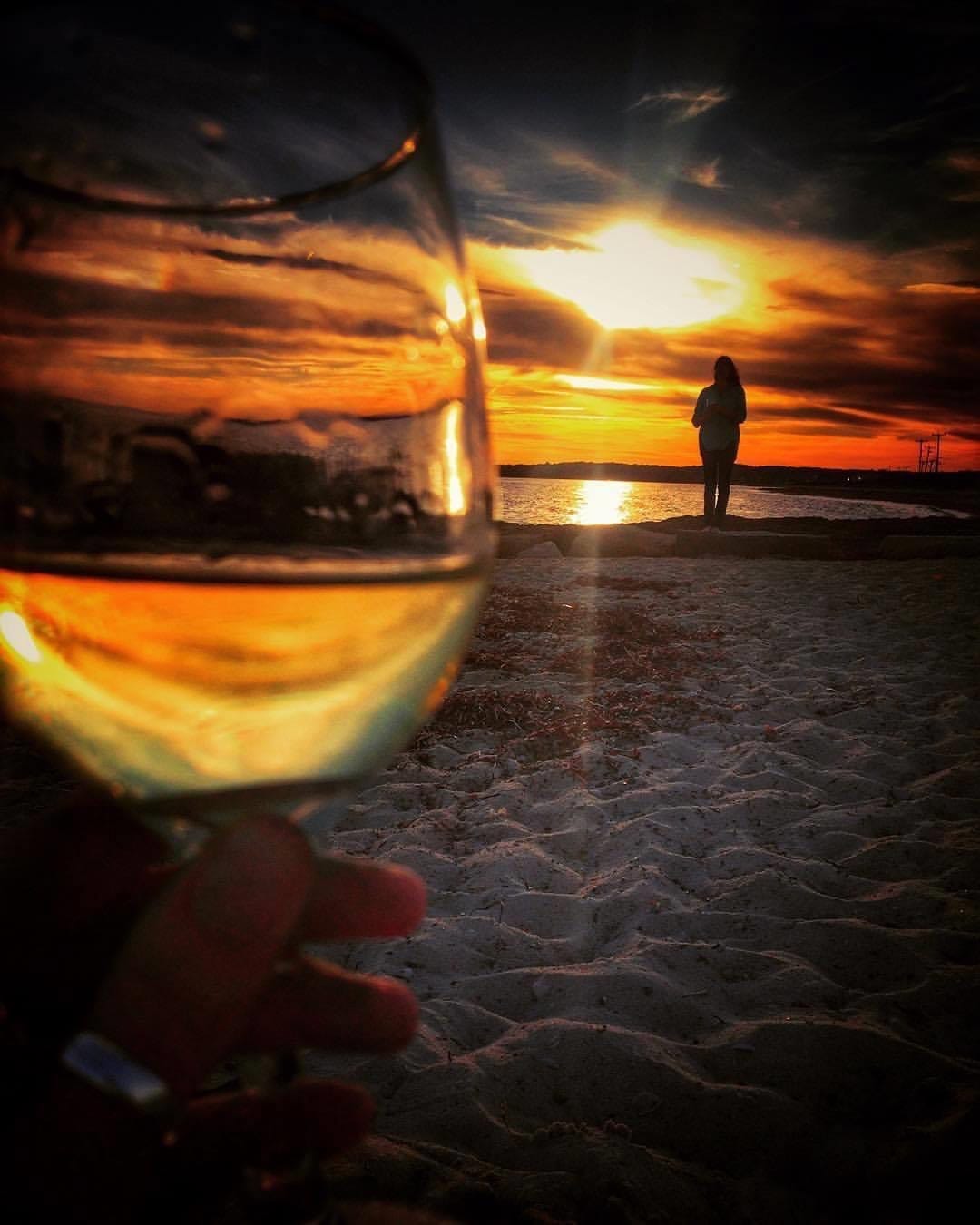 Golden sunset on the beaches of Cape Cod, Massachusetts, with a glass of white wine in the foreground and a silhouette by the water—capturing bespoke coastal escapes, luxury travel experiences, and soulful journeys designed by a boutique travel planner.
