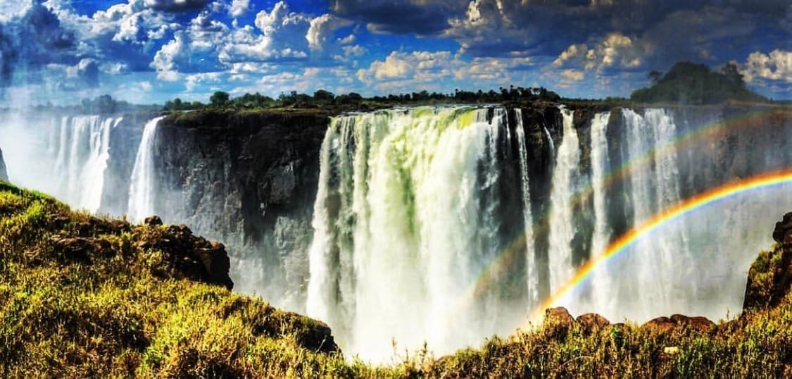 Victoria Falls on the Zambia–Zimbabwe border, with powerful cascades plunging into the gorge beneath a double rainbow—an iconic destination for luxury African travel, bespoke adventure itineraries, and soulful journeys curated by a boutique travel planner.