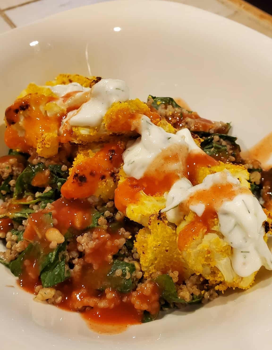 Breaded Cauliflower over seasoned quinoa with cilantro crema and buffalo sauce