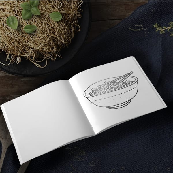 Open coloring book showing a bowl of noodles with chopsticks line art, styled on a dark tabletop with a nest of raw noodles and herbs.