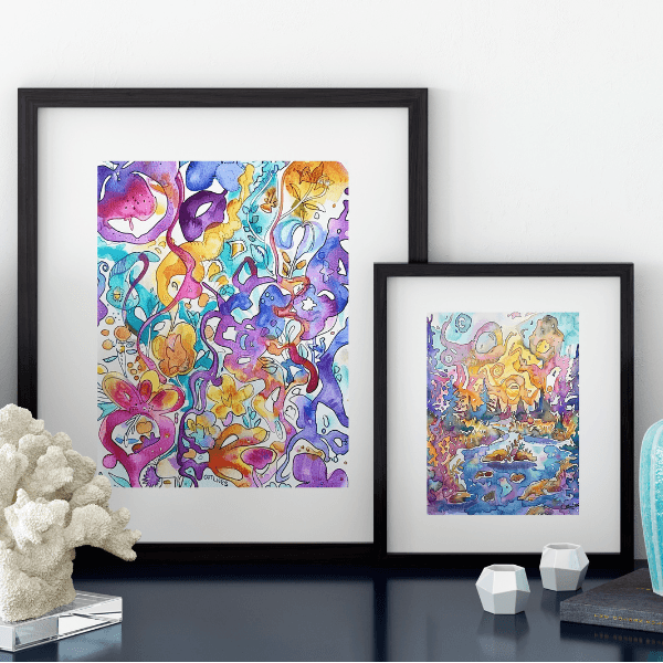 Framed abstract watercolor artworks from the Reverse Coloring Book for Adults displayed on a table. Vibrant printable reverse coloring pages featuring colorful patterns for creativity and relaxation.