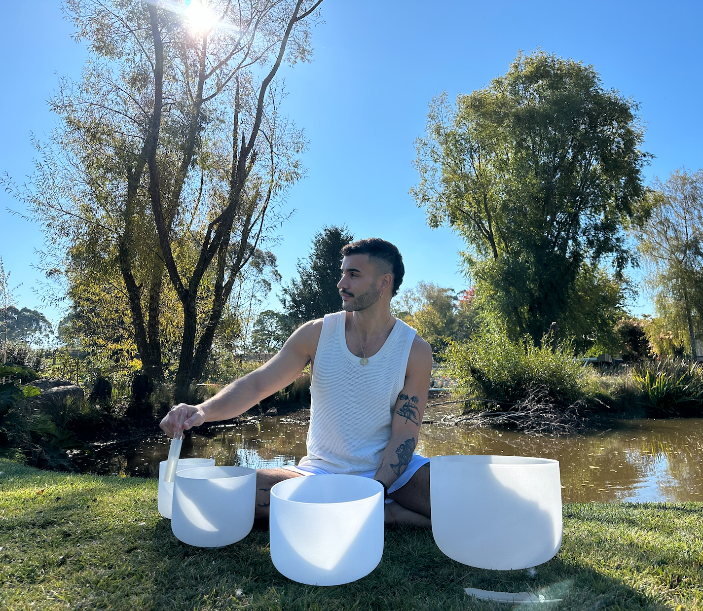 Ange Monitto playing crystal singing bowls on the grass beside a creek
