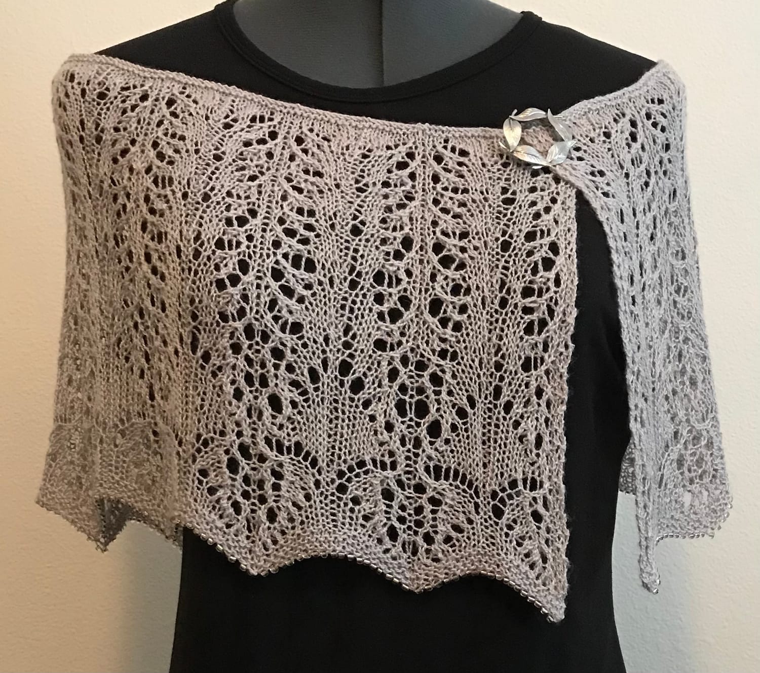 a dress form with a grey capelet draped on it. 