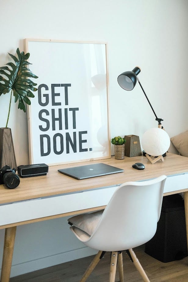 Marketing coaching services workspace with "GET SHIT DONE" poster, laptop, desk lamp, plant, and chair.