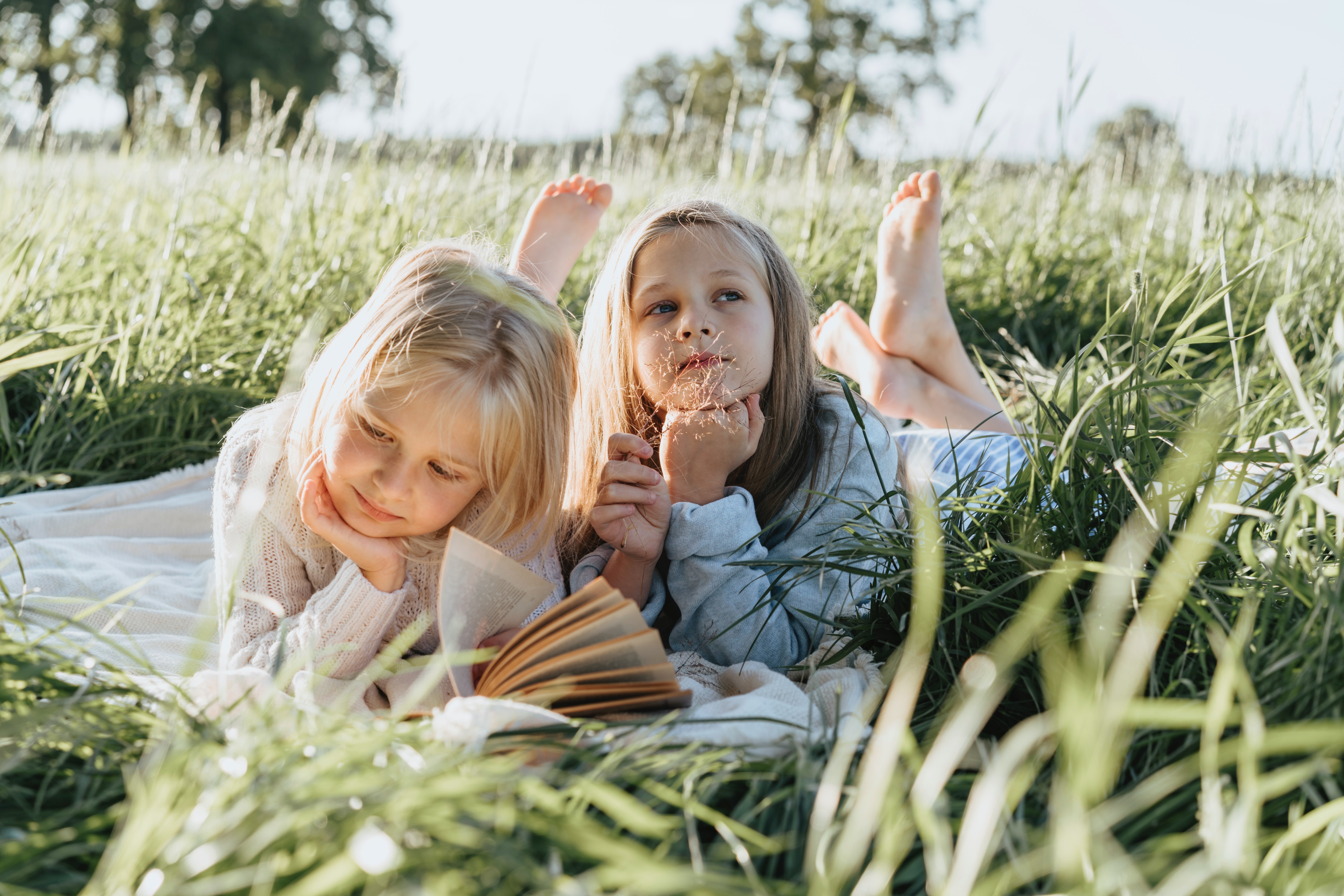 deux enfant dans l'herbe au soleil. L'une lit, l'autre rêvasse 