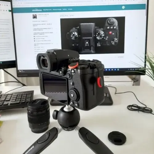 Appareil photo Lumix et objectifs sur un bureau devant un ordinateur allumé diffusant une formation en ligne en photo.