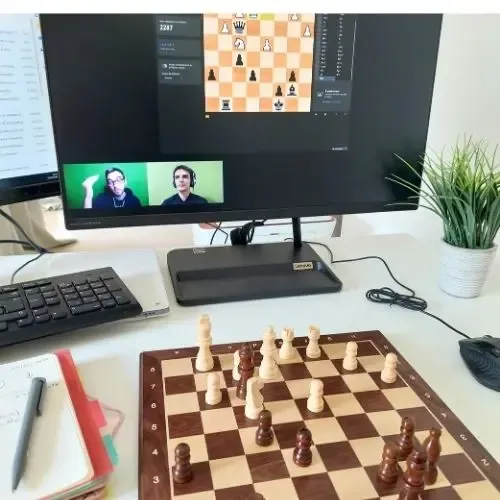 Echiquier sur une table devant un ordinateur qui diffuse une formation en ligne en stratégie de jeux d'échecs.