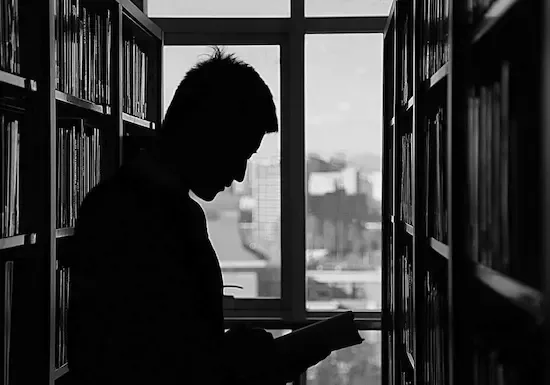 Sileta a contraluz de hombre joven en el pasillo de una biblioteca