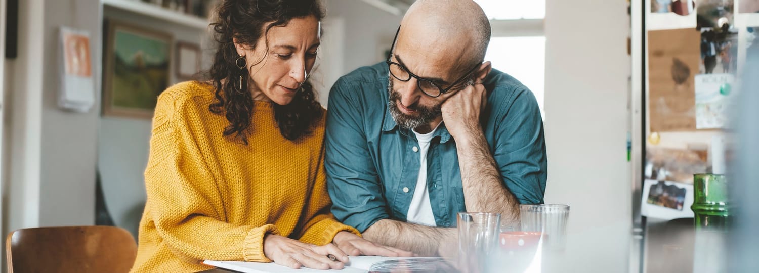 man and woman at kitchen table reading information in a notebook