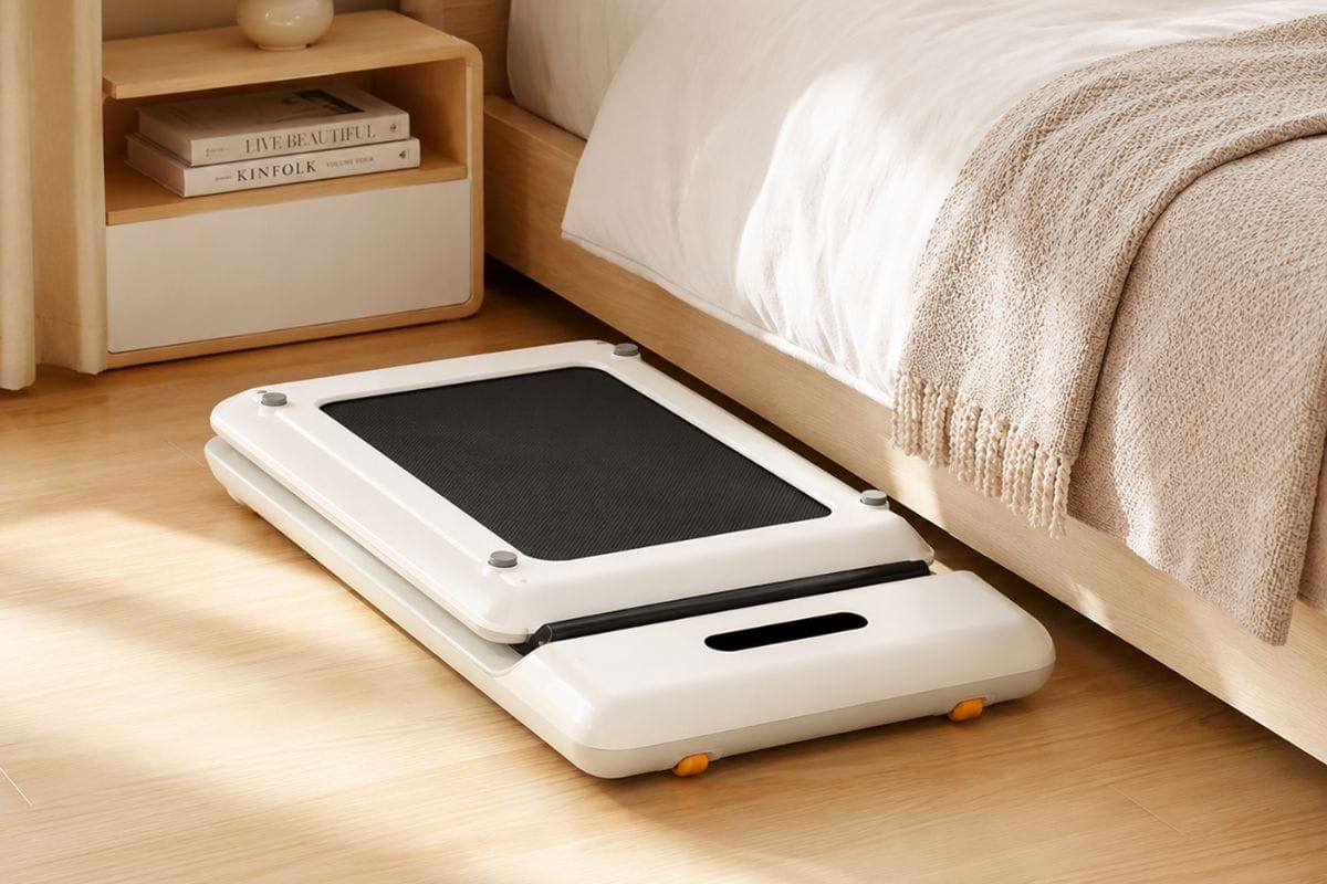 WalkingPad C2 folded flat next to a bed frame in a small apartment bedroom