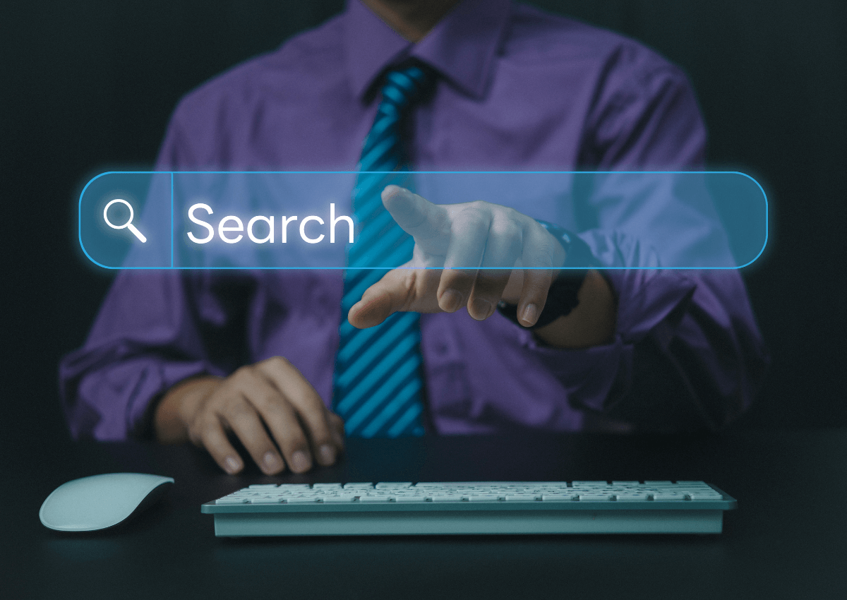 Geschäftsmann im lila Hemd und blauer Krawatte sitzt vor Tastatur und Maus, tippt auf ein schwebendes, transparentes Suchfeld mit dem Wort „Search“. Symbolbild für Online-Suche, digitale Informationsbeschaffung und Suchmaschinenoptimierung.