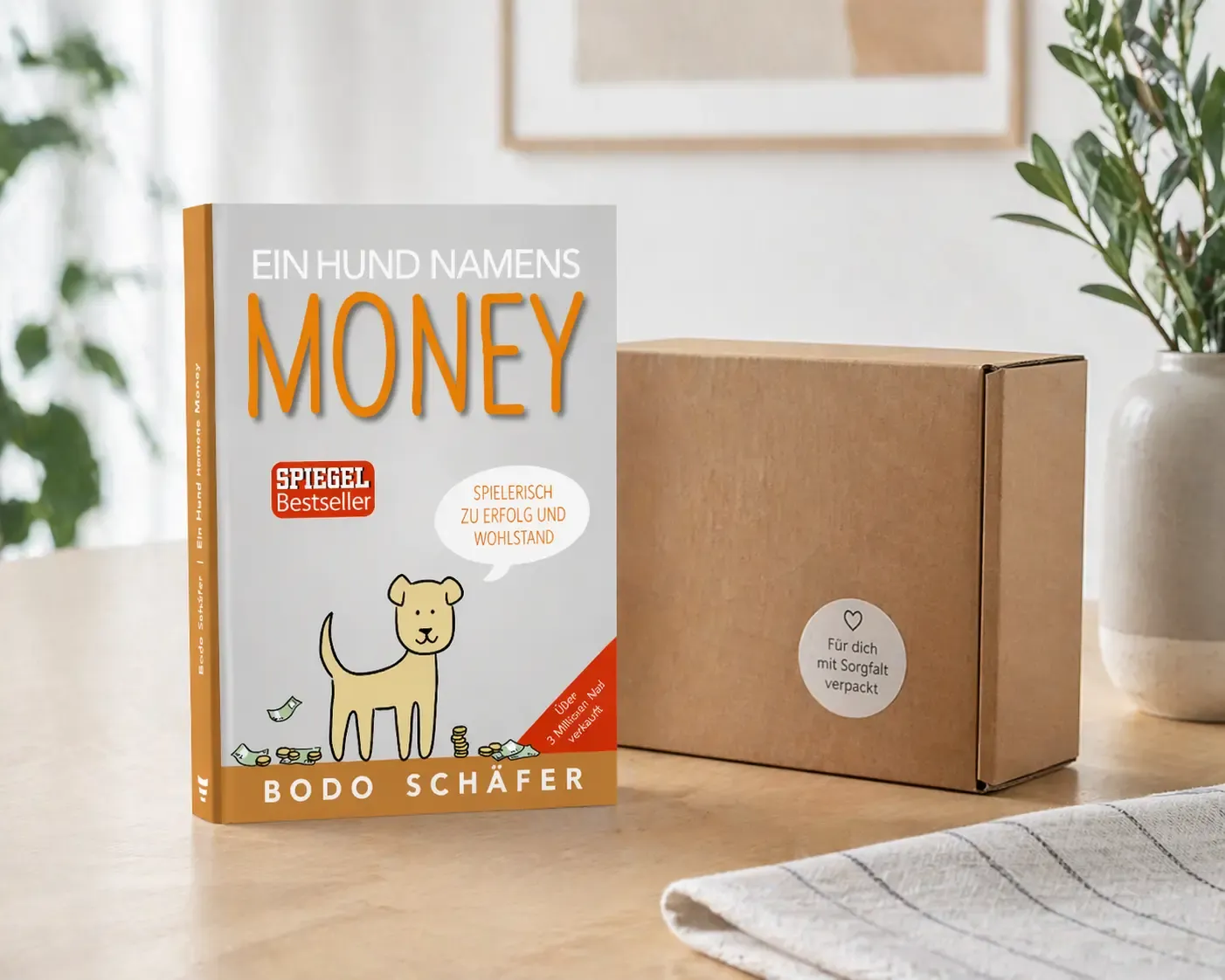 Buch „Ein Hund namens Money“ neben Versandkarton auf hellem Tisch, minimalistisches Produktbild mit natürlichem Licht und sauberer Darstellung