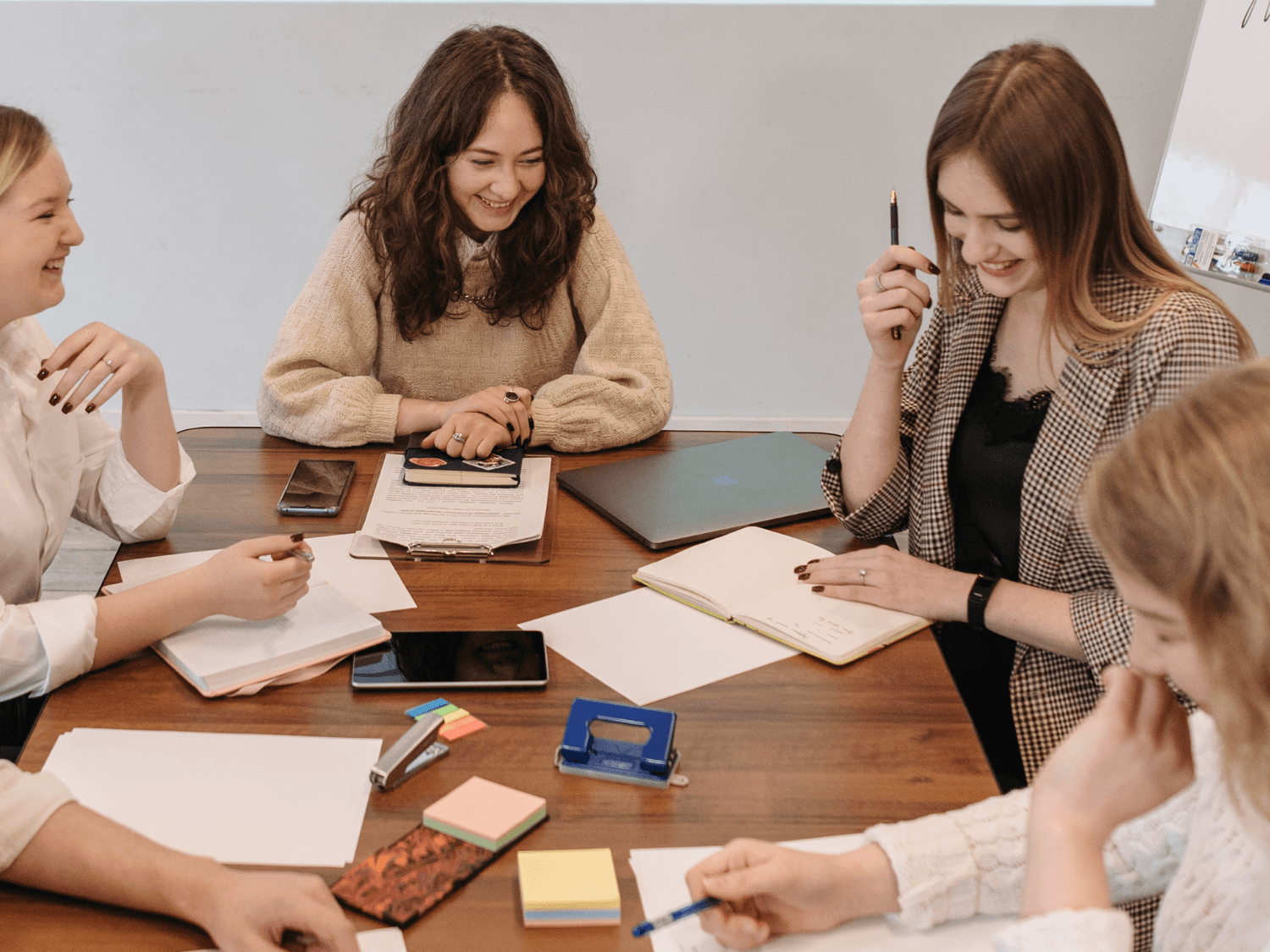 „Grupa kobiet przy stoliku podczas luźnego spotkania warsztatowego — rozmowy, notatki i uśmiechy