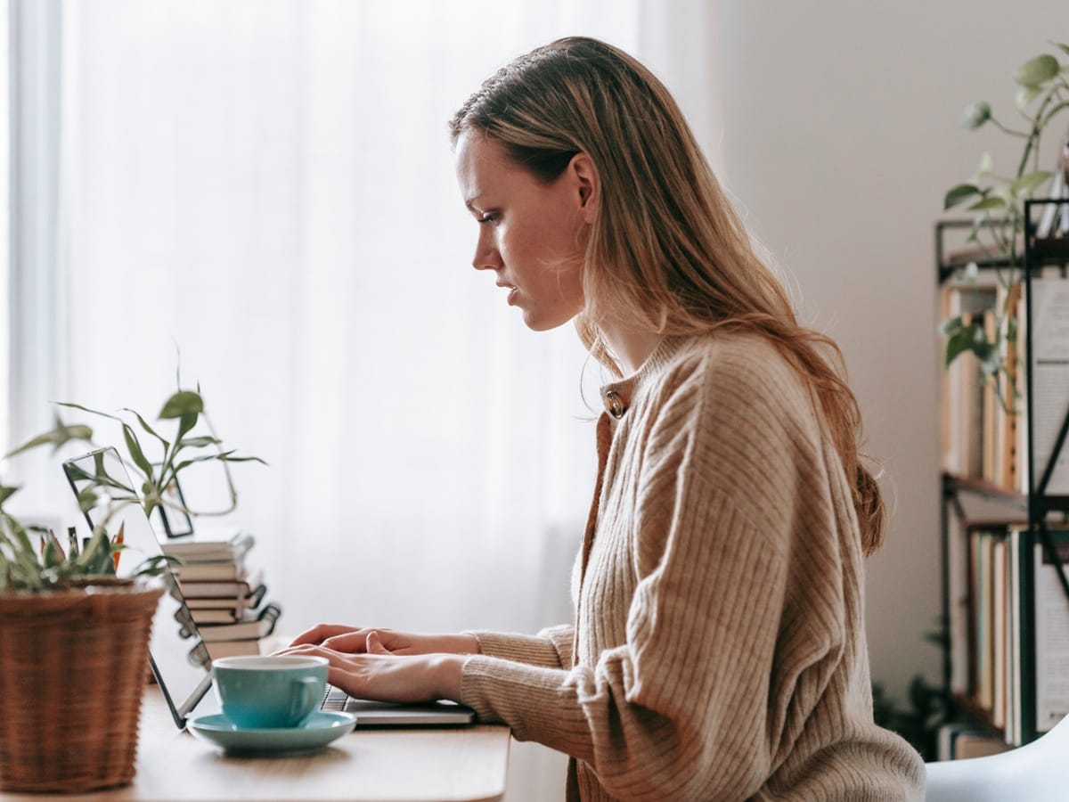 Kobieta pisze na laptopie i analizuje tekst, symbolizując pracę nad odzyskaniem spokoju w finansach.