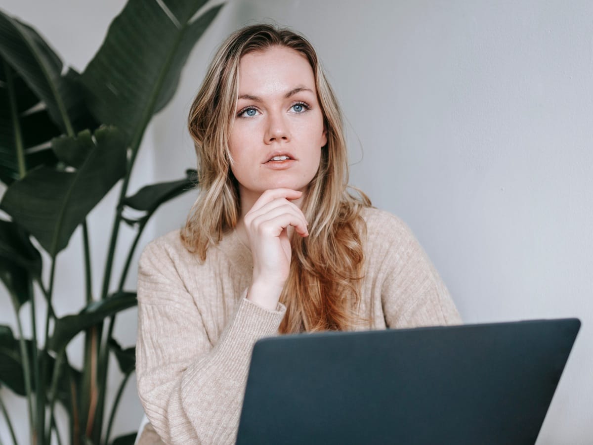 Kobieta siedzi przed laptopem i patrzy w zamyśleniu, symbolizując pierwszy krok w świadomym planowaniu finansów.