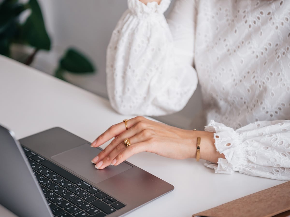 Dłoń kobiety na laptopie w jasnym wnętrzu — ujęcie symbolizujące pracę i naukę podczas webinarów