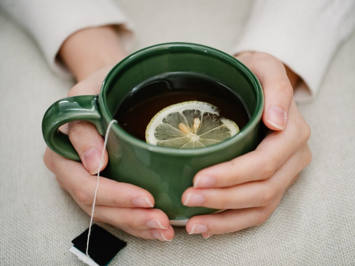 Kobiece dłonie trzymają kubek z gorącą herbatą, symbol chwili zatrzymania i troski o siebie podczas trudnych decyzji życiowych.