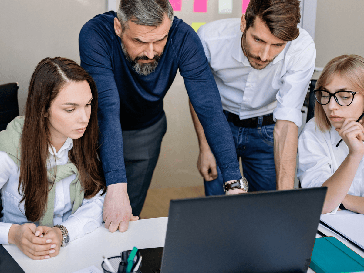 Cztery osoby pochylone nad laptopem, analizujące problem w firmie; widać skupienie i lekki niepokój, sugerujące, że coś wymaga natychmiastowej uwagi.