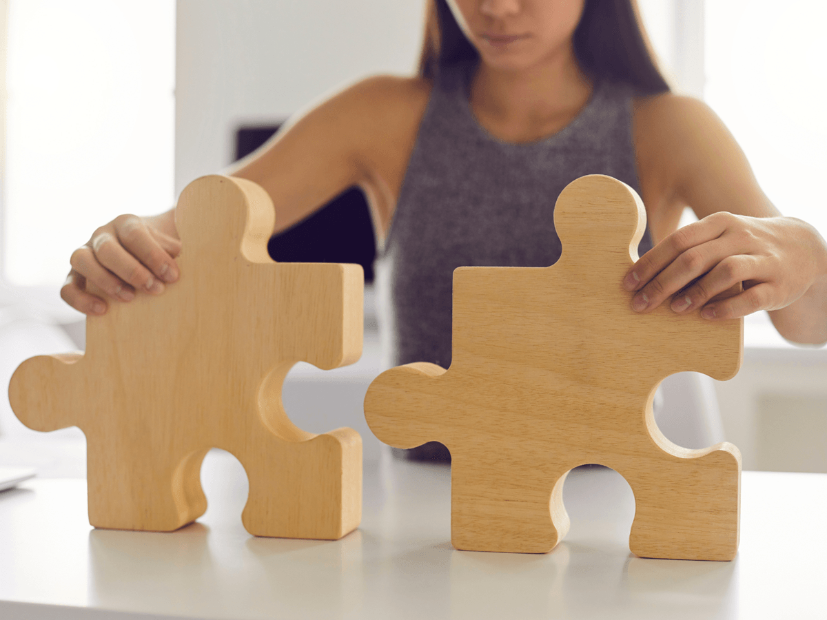 Kobieta składająca dwa drewniane puzzle jako symbol budowania spójnego systemu w firmie