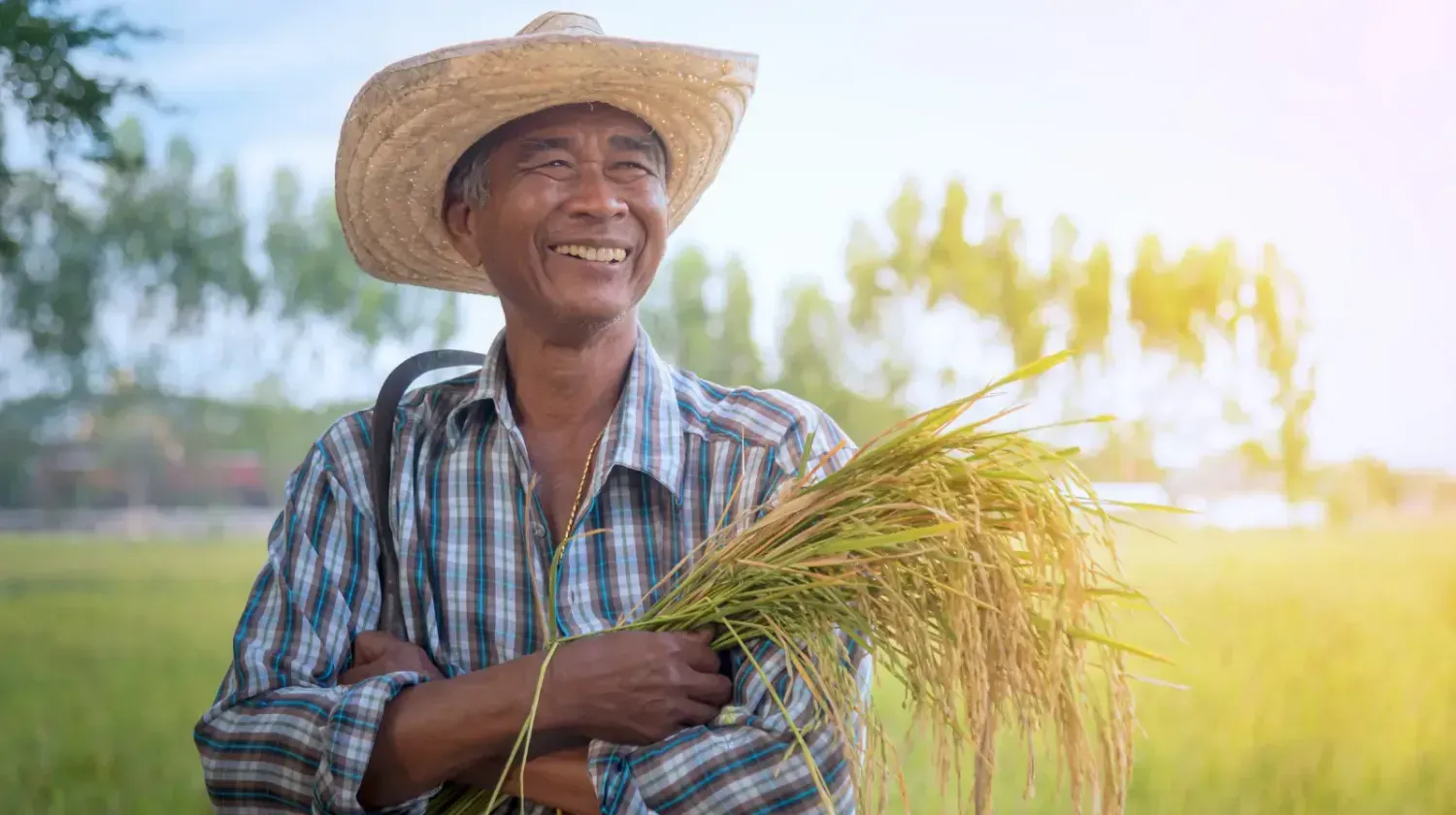 Smiling Thai farmer in a rice field with a straw hat, representing the friendliness of local people.