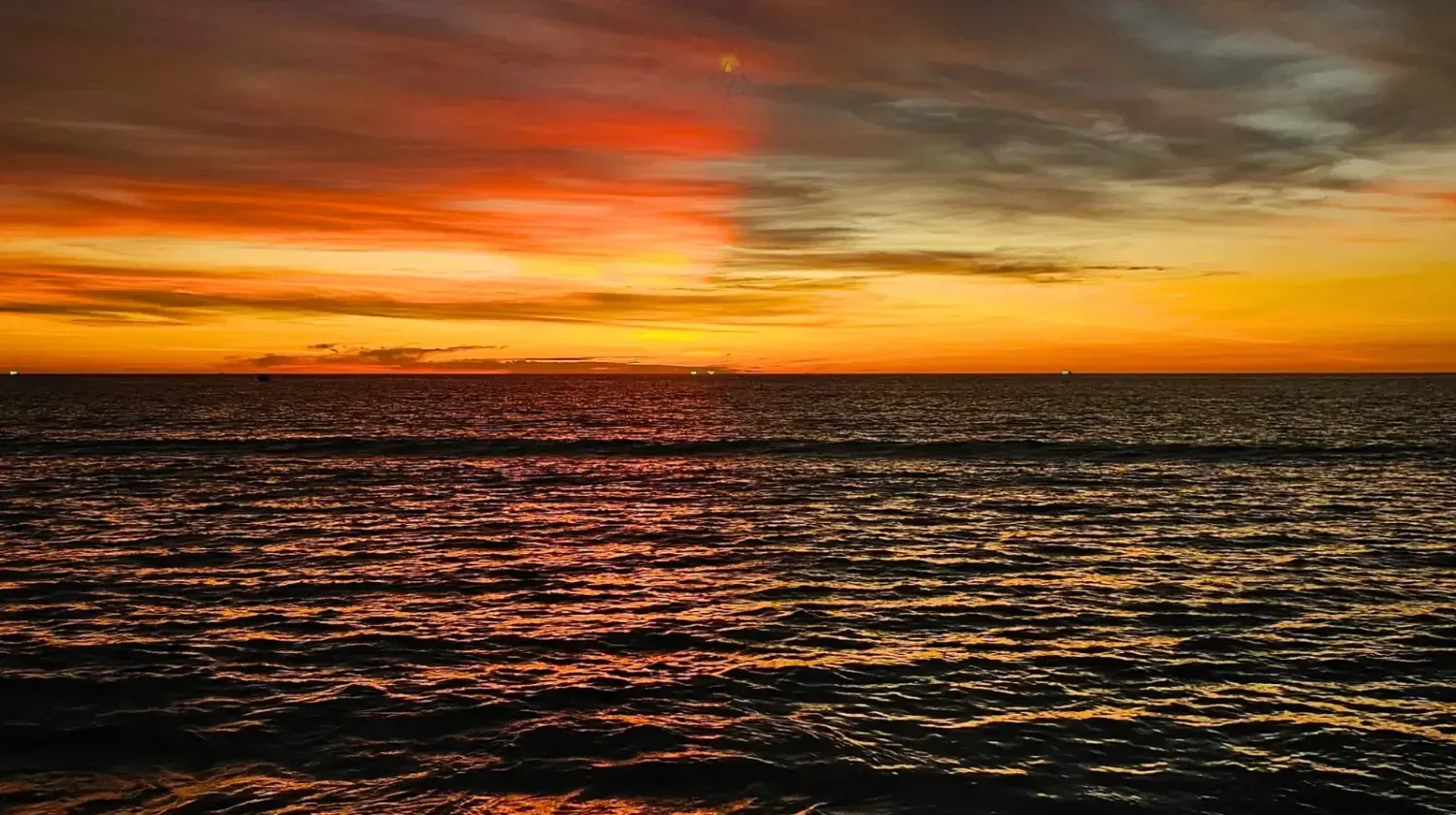 Tropical beach in Thailand with palm trees and ocean at sunset, symbolizing warm weather year-round.