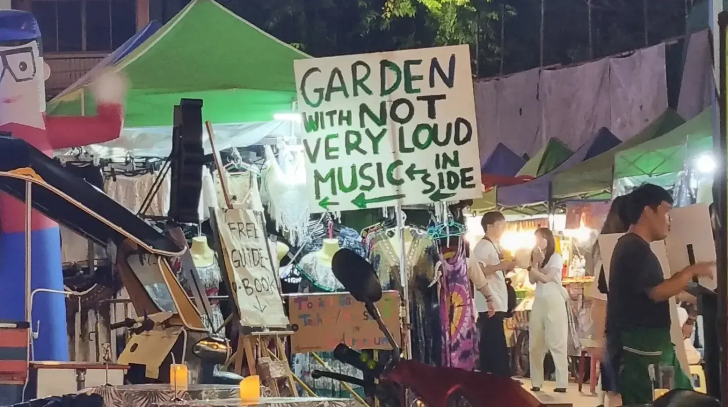 Colorful outdoor market in Thailand with sign about music, representing local culture, fun, and relaxation.