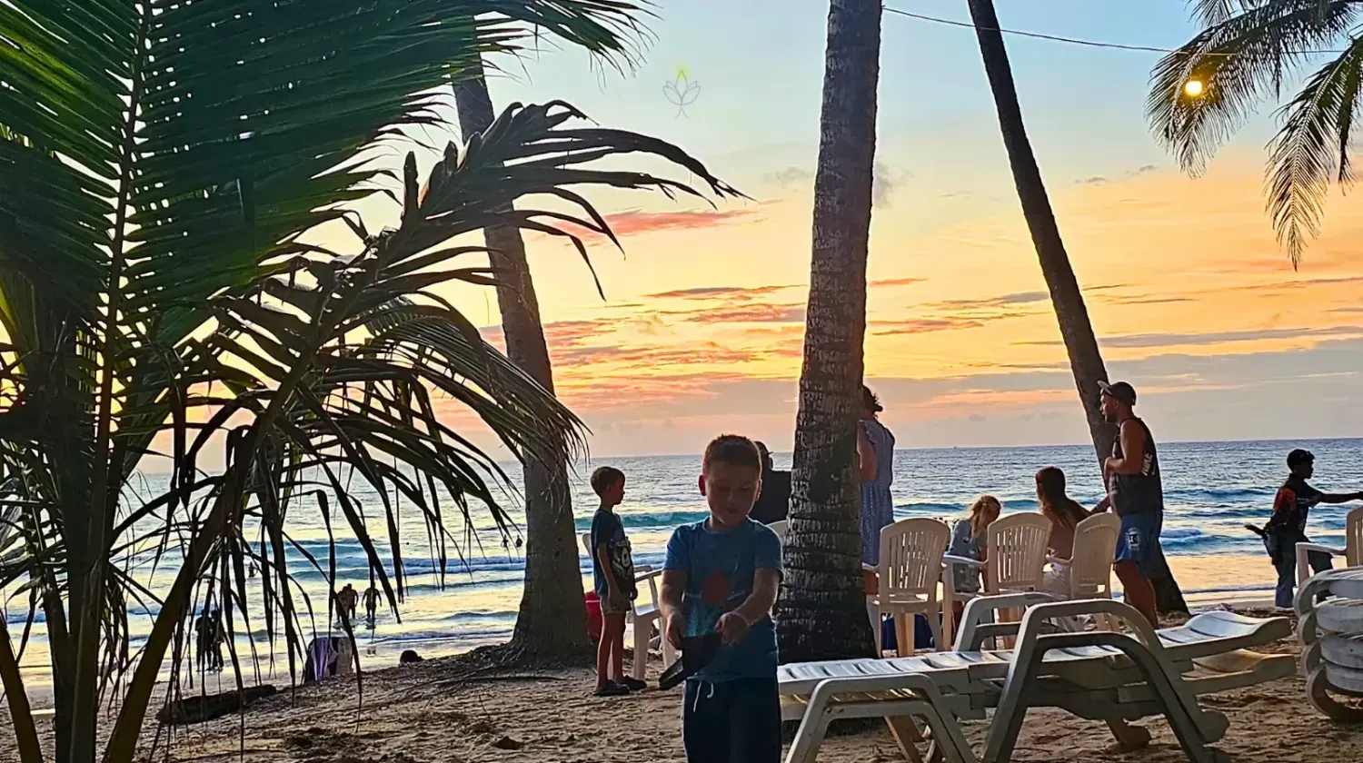 Sunset on a Thai beach with palm trees and people enjoying the view, symbolizing freedom lifestyle.