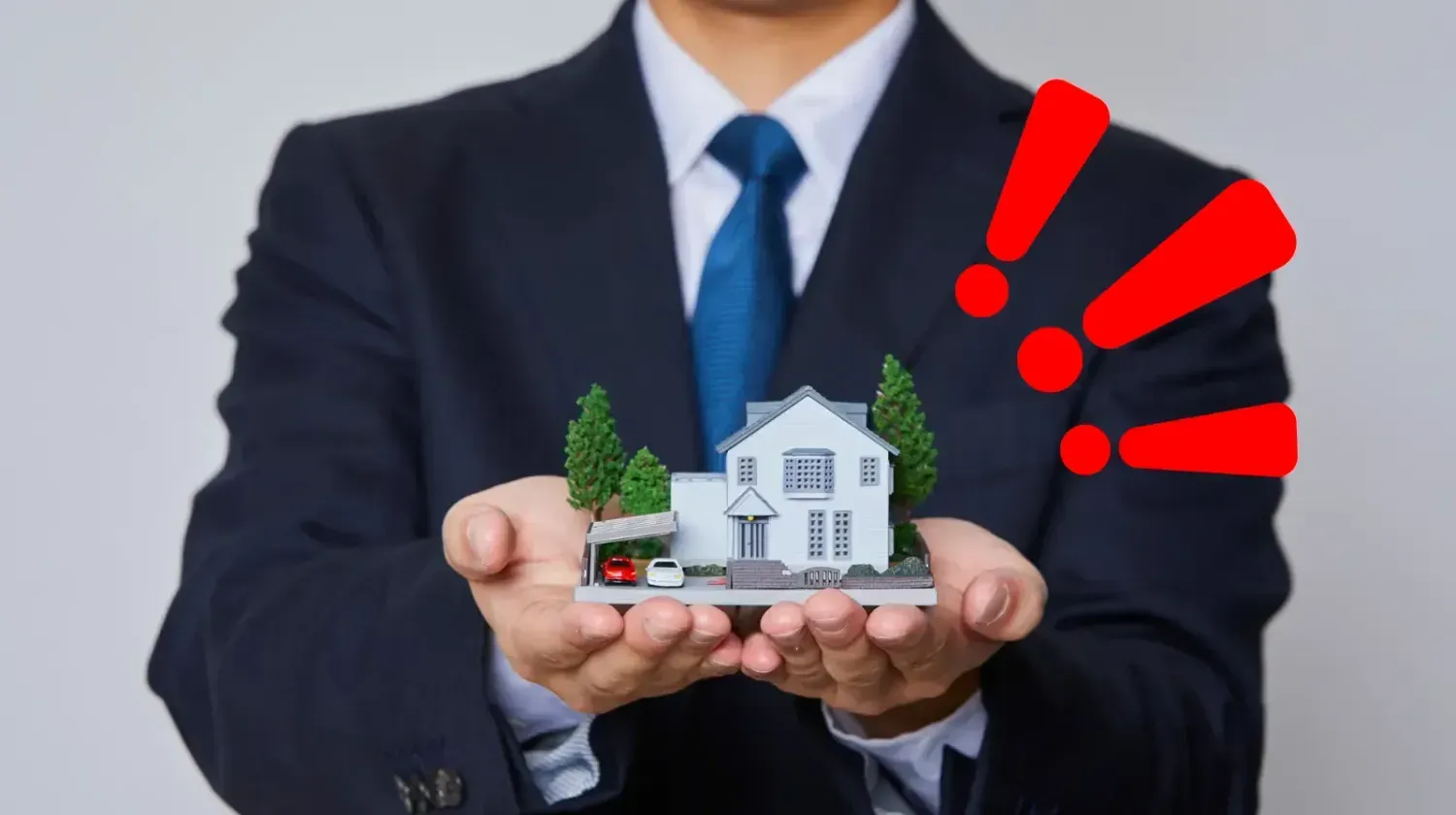Hand holding miniature house with red alert symbols — warning about hidden costs and unrealistic real estate brochures in Dubai property market.