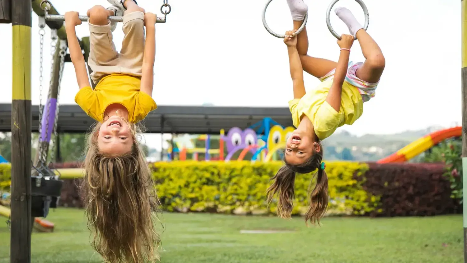 Two happy kids hanging upside down on playground bars, laughing and enjoying travel freedom, representing the Firefly mindset shift.