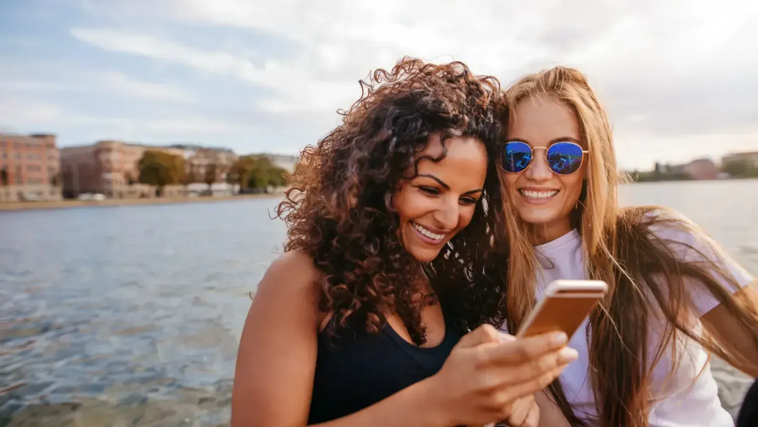 two smiling women looking at a smartphone outdoors, learning and connecting online — showing how to study successful people and build your own Freedom Lifestyle.